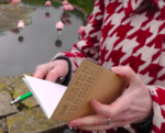 Cropped picture of hands holidng a notebook and pen, red and white graphic jumper, flamingos on water in background